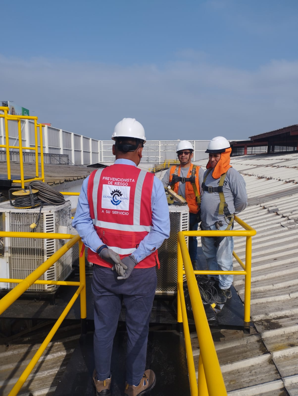 Prevencionista con chaleco de CK Solutions acompañando a dos trabajadores con equipos de protección en una cubierta industrial